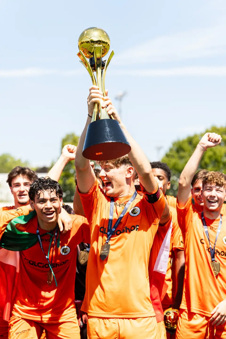 Capitaine en maillot orange brandissant le trophée doré au milieu de son équipe