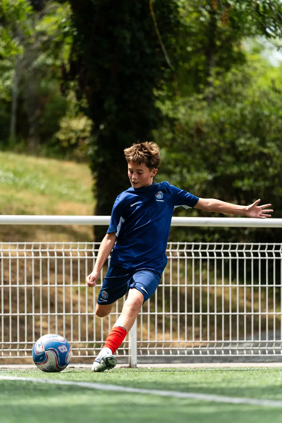 Jeune joueur en maillot bleu frappant le ballon sur un terrain synthétique