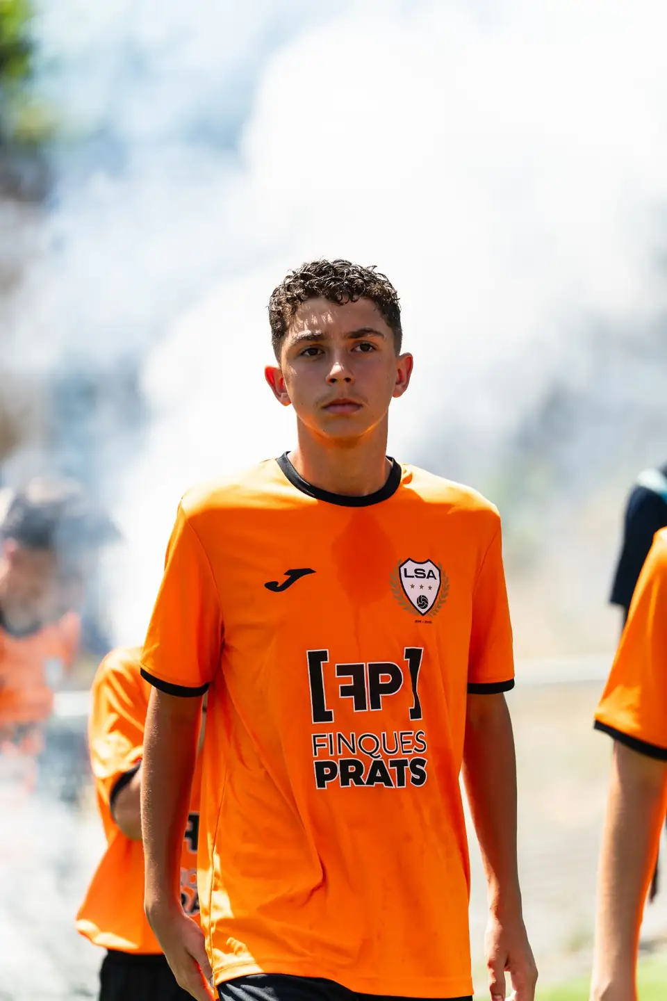 Joueur en maillot orange entrant sur le terrain dans les fumigènes avant un match du tournoi