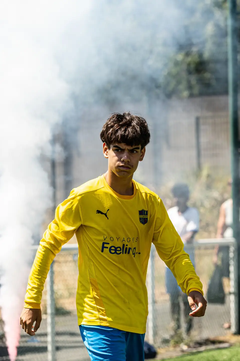 Jeune footballeur en maillot jaune entrant sur le terrain, fumigènes en arrière-plan
