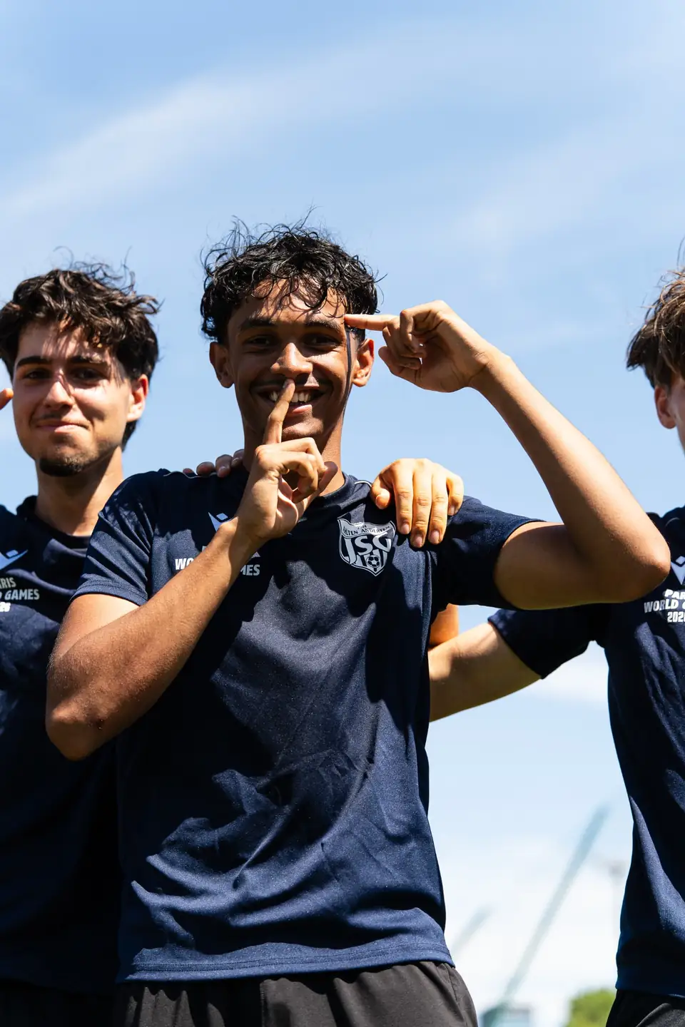 Trois joueurs en maillot bleu marine célébrant, doigt sur la bouche
